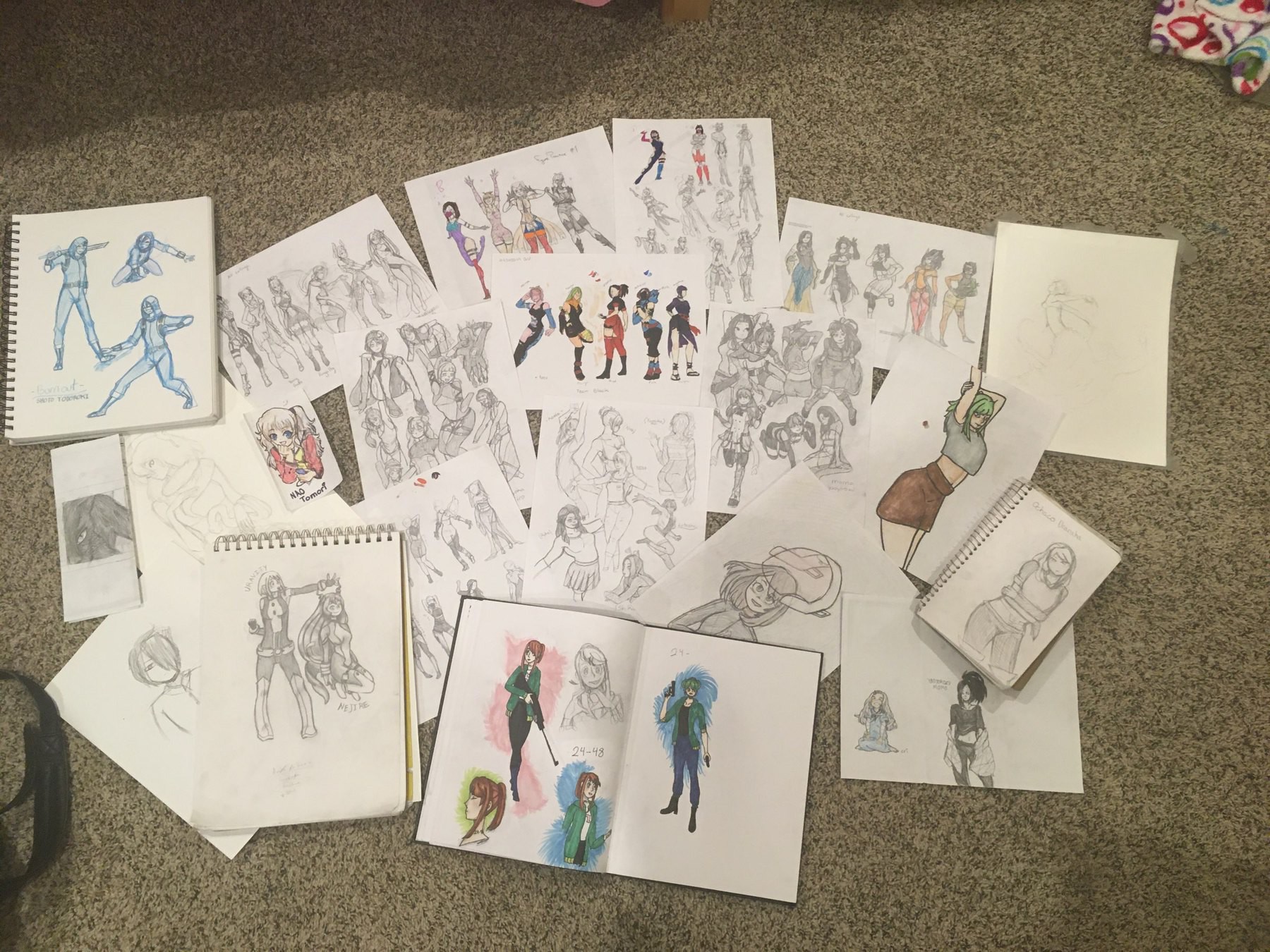 Many pages of sketches and colorings laid out on the floor