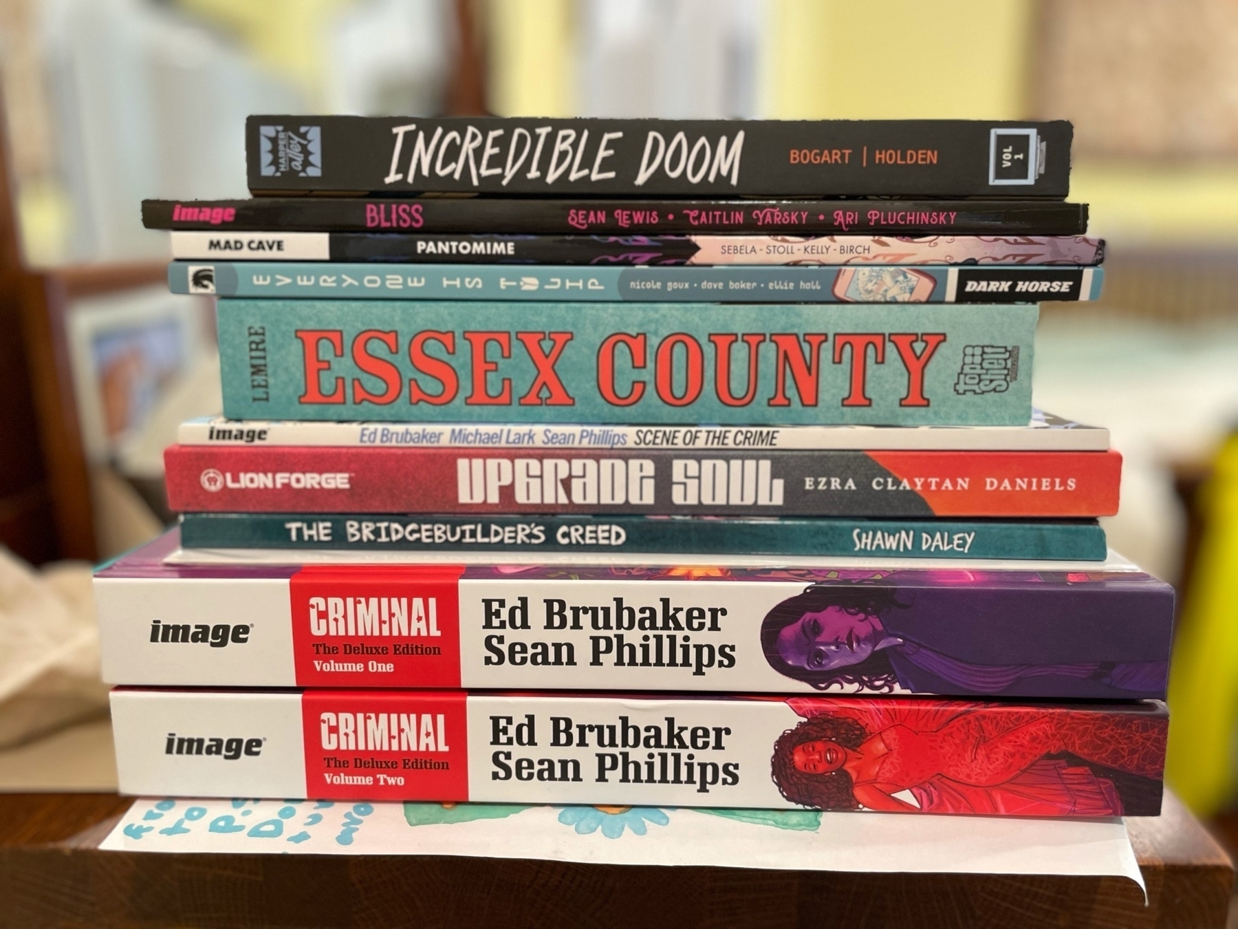 Stack of graphic novels, top to bottom: Incredible Doom, Bliss, Pantomime, Everyone Is Tulip, Essex County, Scene of the Crime, Upgrade Soul, The Bridgebuilder's Creed, Criminal Deluxe Editions Volumes 1 and 2