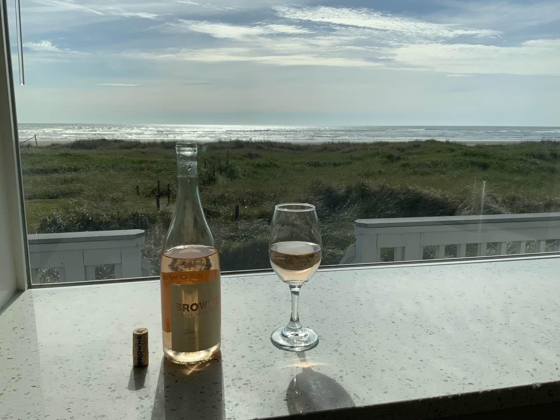 Bottle and glass of rosé wine on the counter, overlooking dunes ontk the ocean 