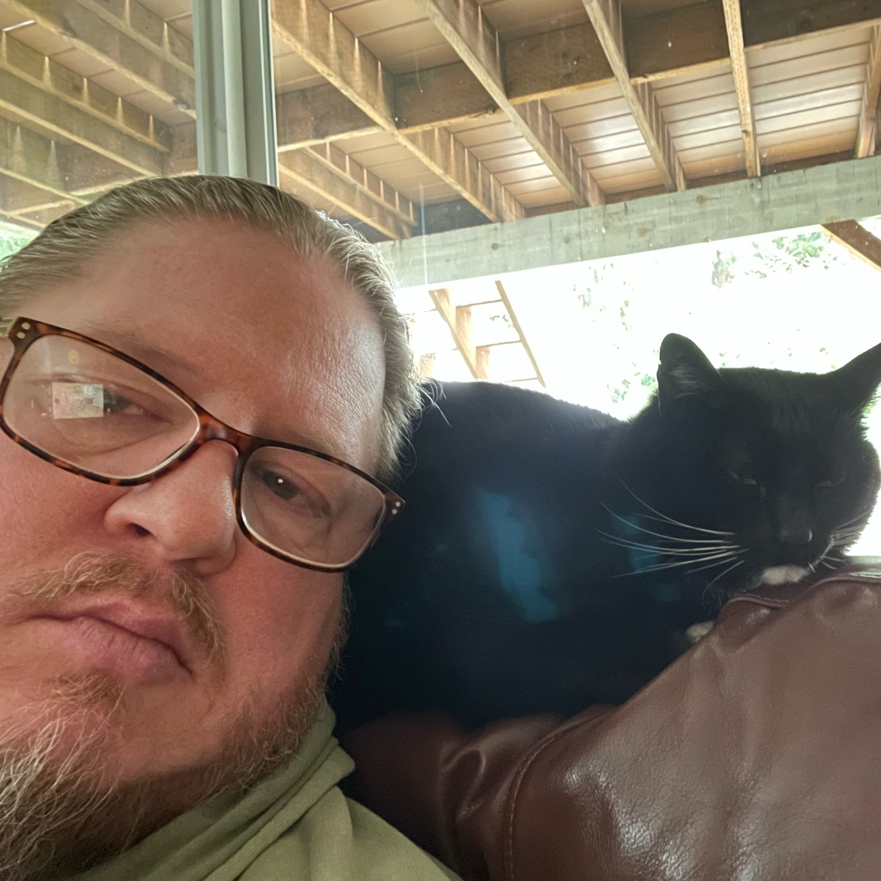 Selfie of me leaning up against our black tuxedo cat on the back of the armchair