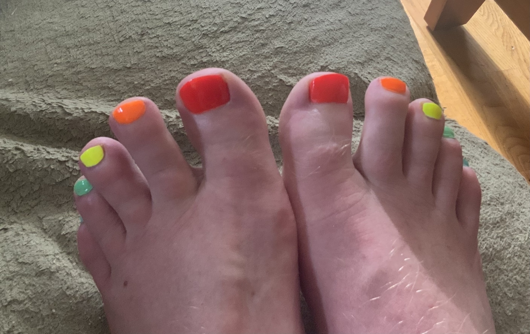 post-pedicure feet with nail polish of neon red, orange, yellow, green, and blue